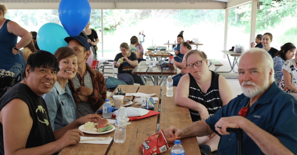 A group of people seated at a picnic table smiling.