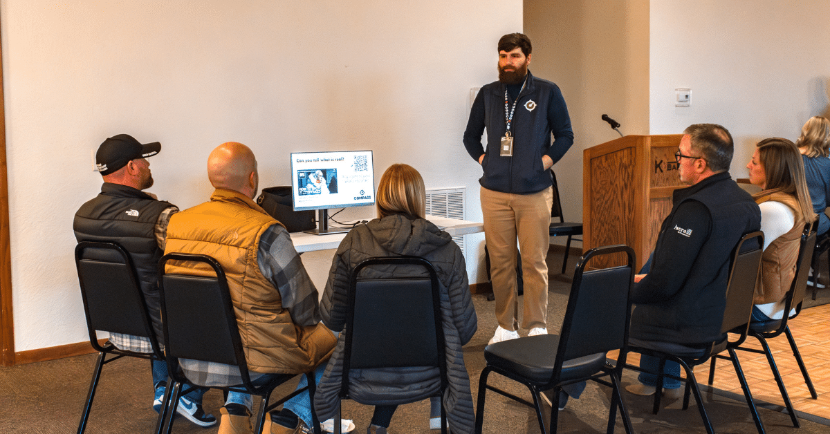 Man standing in front of a computer presenting to a seated group of five people.